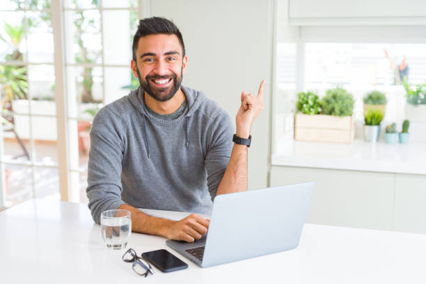 istock Handsome hispanic man working using computer laptop very happy pointing with hand and finger to the side 1143702159