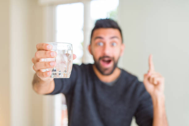 istock Handsome hispanic man drinking a fresh glass of water surprised with an idea or question pointing finger with happy face, number one 1143702167