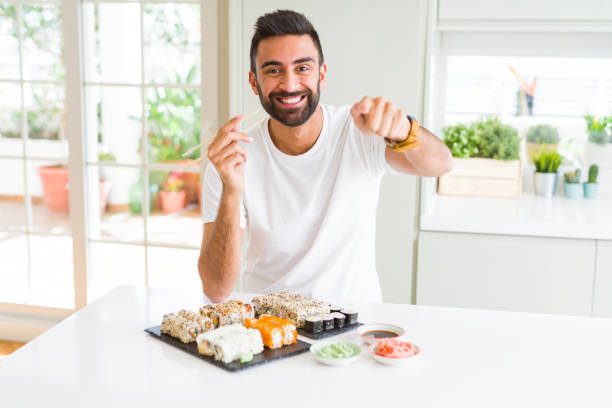 istock Handsome hispanic man eating asian sushi using chopsticks pointing with finger to the camera and to you, hand sign, positive and confident gesture from the front 1143703149