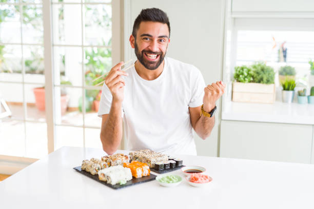 istock Handsome hispanic man eating asian sushi using chopsticks screaming proud and celebrating victory and success very excited, cheering emotion 1143703159