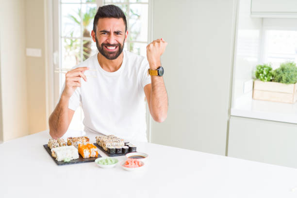 istock Handsome hispanic man eating asian sushi using chopsticks annoyed and frustrated shouting with anger, crazy and yelling with raised hand, anger concept 1143703177