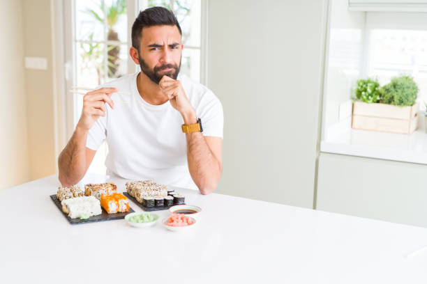 istock Handsome hispanic man eating asian sushi using chopsticks serious face thinking about question, very confused idea 1143703179