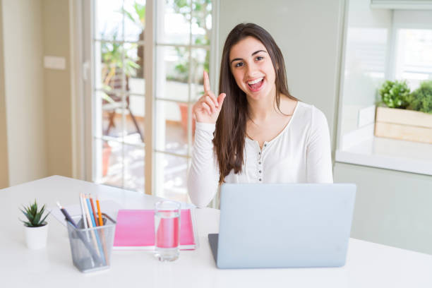 istock Beautiful young student woman studying for university using laptop and notebook surprised with an idea or question pointing finger with happy face, number one 1143703274