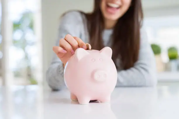 Photo of Young woman smiling putting a coin inside piggy bank as savings for investment