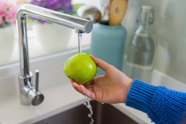 istock Young woman washing vegetables and fruit using water from sink 1143703850