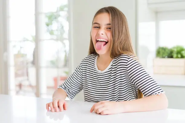 Photo of Beautiful young girl kid wearing stripes t-shirt sticking tongue out happy with funny expression. Emotion concept.
