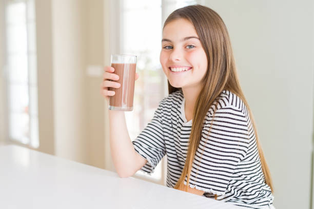 beau gosse de jeune fille buvant le milkshake délicieux de chocolat frais comme collation avec un visage heureux debout et souriant avec un sourire confiant montrant des dents - toothy smile relaxation white healthcare and medicine photos et images de collection