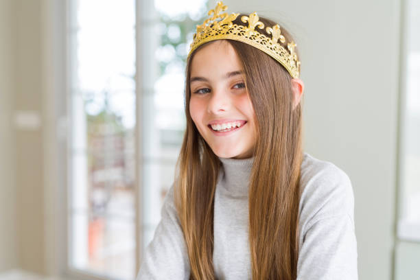 カメラを見て交差腕で微笑んでおとぎ話の幸せな顔から王女として黄金の王冠を着て美しい若い女の子。肯定的な人。 - princess queen nobility crown ストックフォトと画像