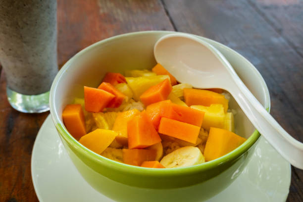 Fresh tropical fruit salad on a plate including mango, banana, pineapple papaya on a wooden table.