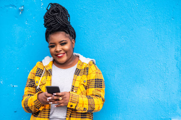 afro kobieta za pomocą smartfona na niebieskim tle - braided women sensuality portrait zdjęcia i obrazy z banku zdjęć