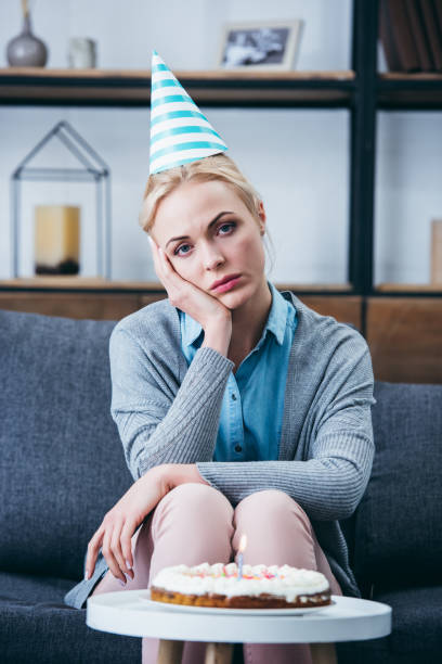 istock sad woman in party hat propping head with hand and looking at camera while celebrating birthday at home alone 1143708644