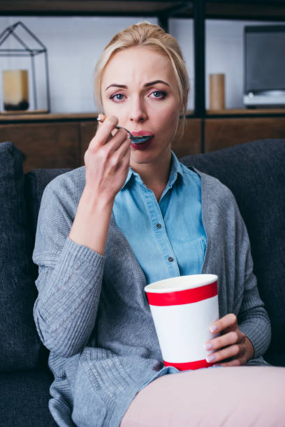 istock sad woman looking at camera and eating ice cream while siitng on couch at home alone 1143709347