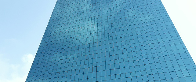 Tall building with a blue glass facade reflecting the clouds in the sky.