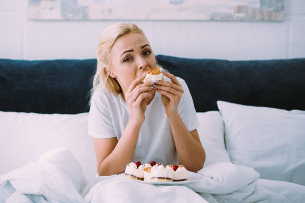 istock upset woman in pajamas looking at camera while eating cake in bed alone 1143709643