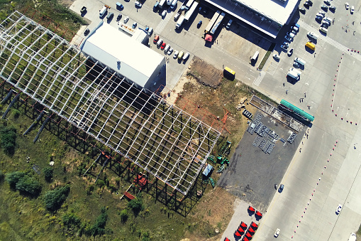Steel frame construction of modern storage warehouse building at big city suburb. Aerial drone view from above.