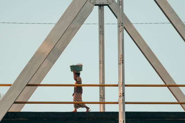 femme portant le panier lourd sur la tête. traverser le pont - porter sur la tête photos et images de collection