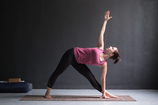 Beautiful young woman working out doing yoga or pilates exercise. Girl standing in Utthita Trikonasana, extended triangle pose.