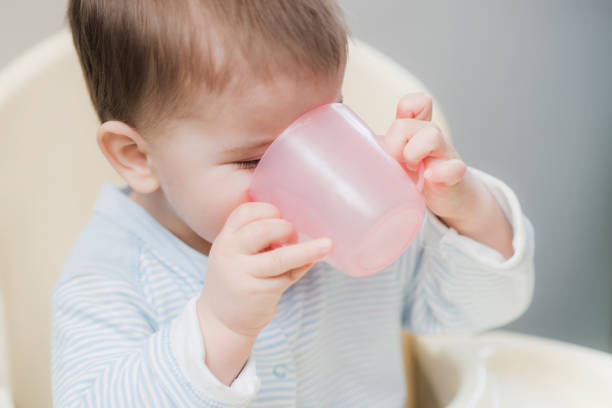 bambino in cucina bevendo da una tazza d'acqua - baby cup foto e immagini stock