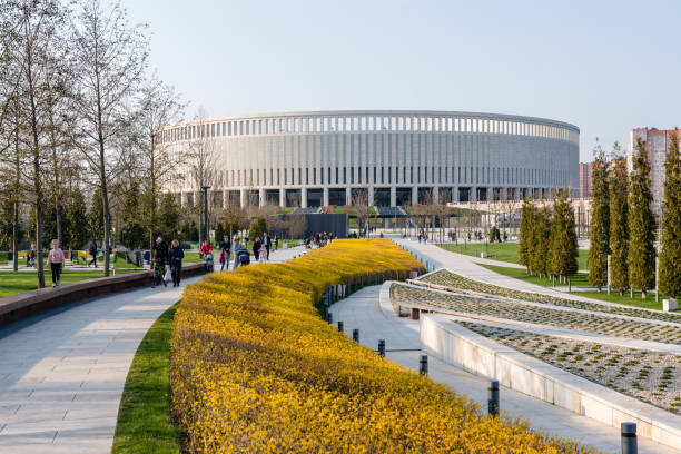 Stadium Krasnodar with a facade of travertine on a background of clean blue sky. In the foreground are beautiful yellow shrubs and walking stone terraces. Krasnodar, Russia - April 5, 2019: Stadium Krasnodar with a facade of travertine on a background of clean blue sky. In the foreground are beautiful yellow shrubs and walking stone terraces. krasnodar stock pictures, royalty-free photos & images