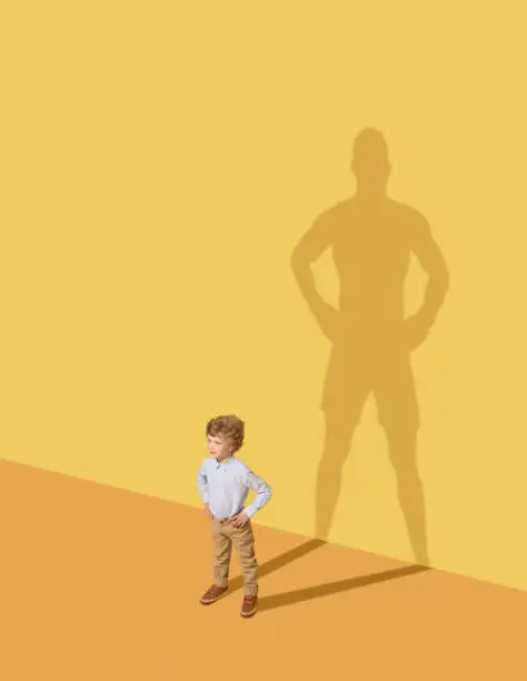 I could protect my family. Future champion. Childhood and dream concept. Conceptual image with child and shadow on the yellow studio wall. Little boy want to become a boxer and to build a sport career.