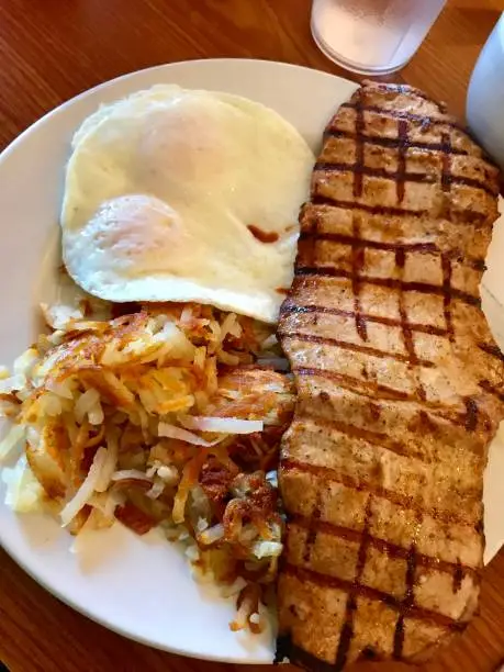 Pork tenderloin, eggs and hash browns for breakfast on a plate.
