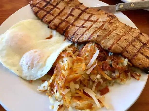 Pork tenderloin, eggs and hash browns for breakfast on a plate.