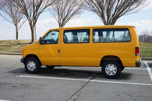 An empty yellow school van sits empty and parked in a parking lot.