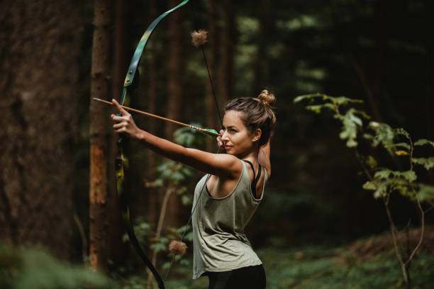 Young female archer practicing in the woods. Female hunter hunting in the forest by herself during the. stock photo