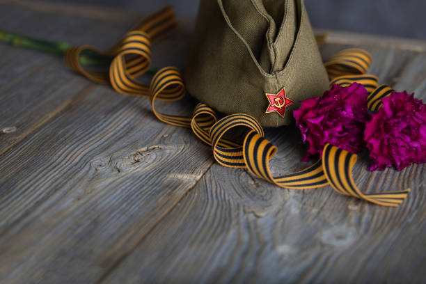 istock Military cap, carnations, Saint George ribbon on a wooden surface. 1143729259