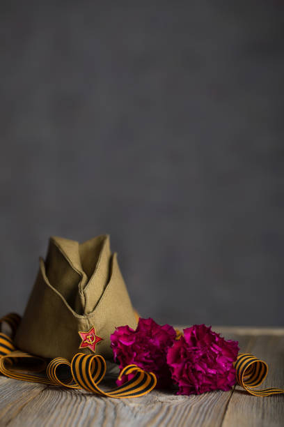 istock Military cap, carnations, Saint George ribbon on a wooden surface. 1143729307
