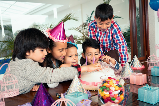 beautiful Latino children celebrate the birthday of the younger cousin and introduce their fingers to the cake demonstrating their great happiness