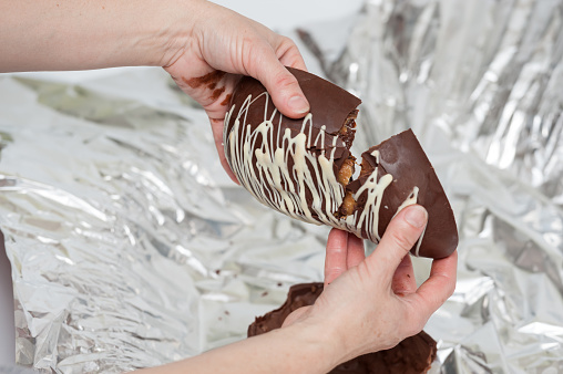 Woman's hands breaking an Easter Egg stuffed with truffles. Background silver packaging. Close-up.