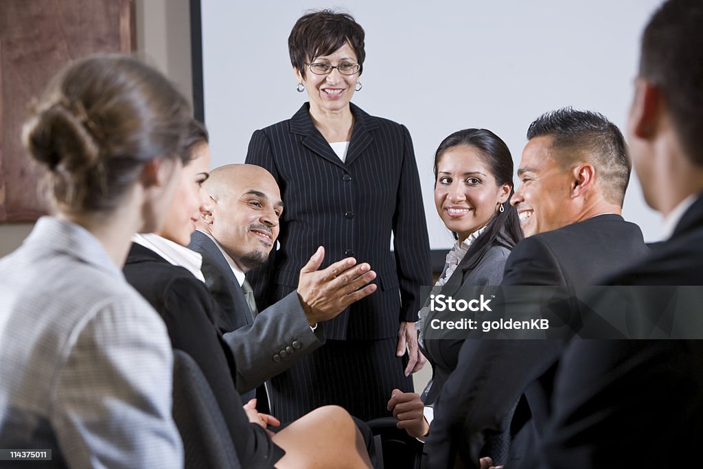 Diverse businesspeople conversing, woman at front Diverse group of businesspeople in meeting or seminar.  Focus on man gesturing and woman sitting across from him. Business Stock Photo