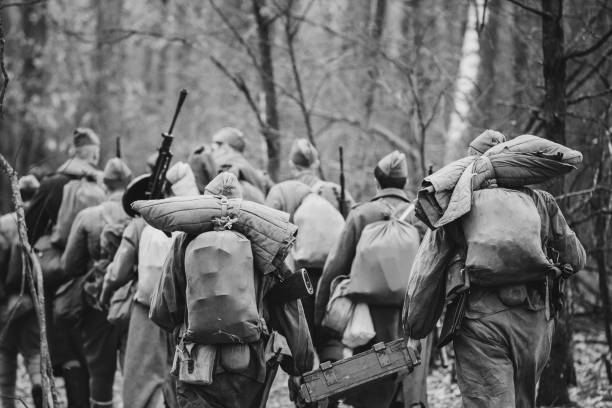 Re-enactors Dressed As World War II Russian Soviet Red Army Soldiers Marching Through Forest In Autumn Day. Photo In Black And White Colors. Soldier Of WWII WW2 Times Re-enactors Dressed As World War II Russian Soviet Red Army Soldiers Marching Through Forest In Autumn Day. Photo In Black And White Colors. Soldier Of WWII WW2 Times. former soviet union stock pictures, royalty-free photos & images