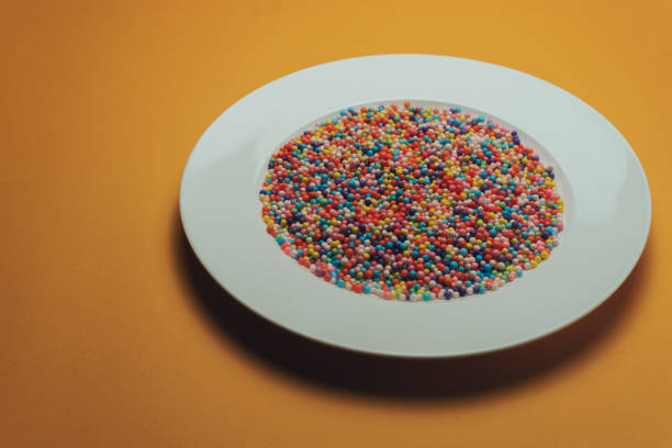 istock White plate with color preparations (vitamins, dyes, flavor enhancers, nutritional supplements, innovative technologies, candy sweets) on an orange background. 1143762035