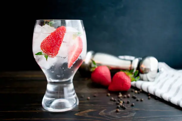 Gin and tonic garnished with strawberries and black pepper