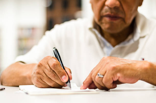 istock Serious senior man sitting on a library bench writing in his book. 1143771540