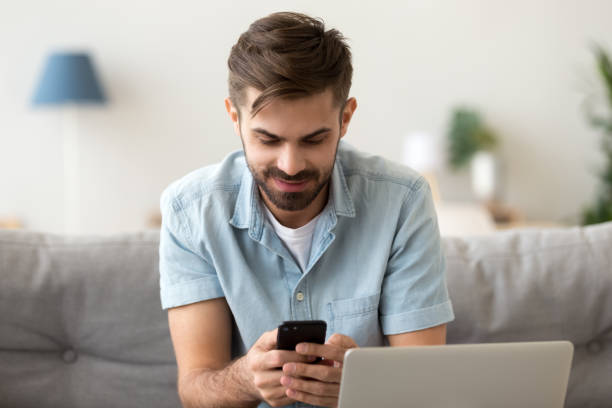 istock Smiling man sitting at home, using phone, chatting, typing message 1143775401