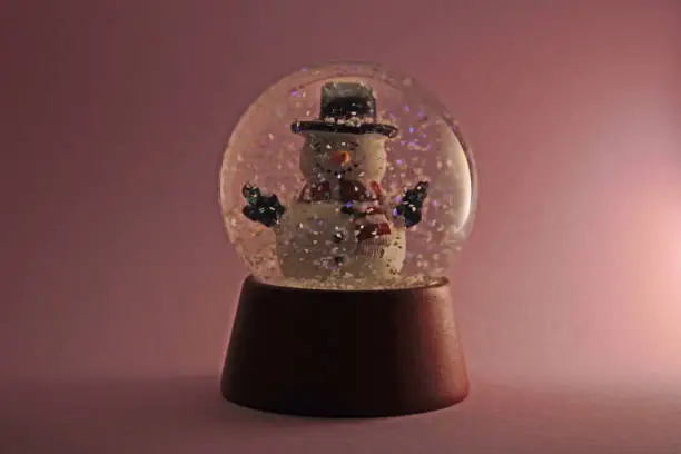 This snowman in a glass dome is surrounded by snowflakes swirling around like a snowstorm. Isolated on pink background.