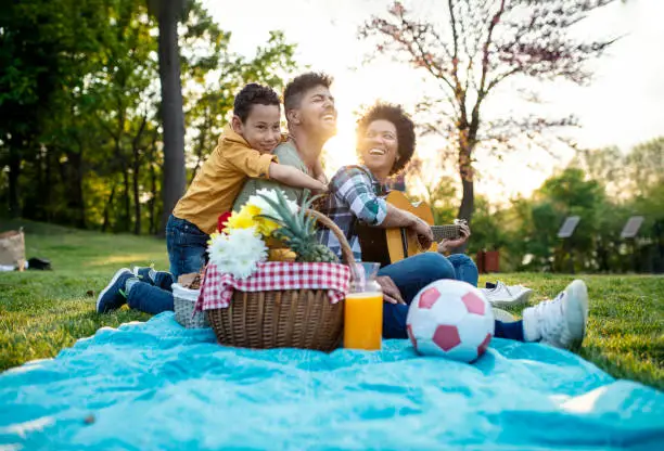 Happy family play guitar and sing together while sitting in the park in summer.