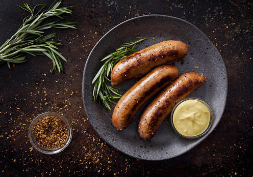 Three sausages in a plate with a side of dijon mustard sauce and seasoning