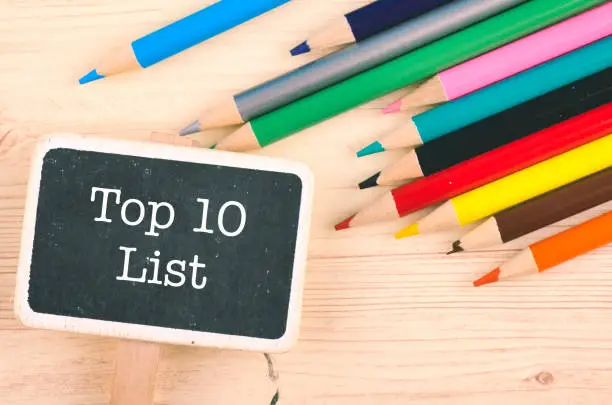 Photo of word TOP 10 LIST written on wooden signage over colorful pencil on desk