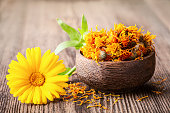 Dried and fresh marigold (calendula) flowers in a bowl on wooden rustic background space for text close-up.