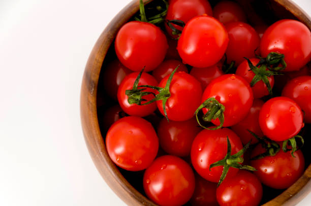 istock Fresh red cherry tomatoes in wooden round bowl on white background 1143856164
