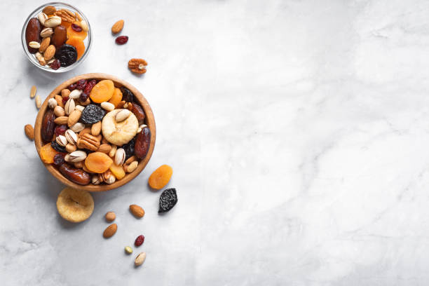 Mixed nuts and dried fruits Mixed nuts and dried fruits in wooden bowl on white marble background, copy space. Healthy snack - mix of organic nuts and dry fruits. dried fruit stock pictures, royalty-free photos & images