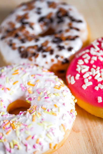 istock Pink, white and brown glazed donuts on wooden background. 1143876167