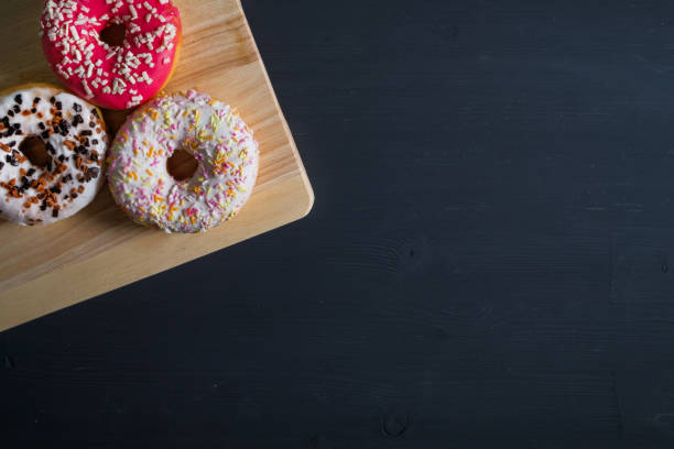istock White, pink and brown glazed donuts in left side on black wooden background. 1143876178
