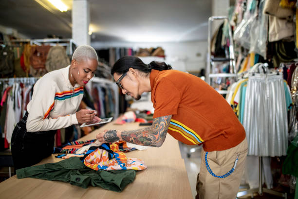 Colleagues using tablet PC while checking textile Businesswoman using digital tablet while checking textile with colleague. Male and female professionals are working at desk. They are standing in design studio. fashion designer stock pictures, royalty-free photos & images