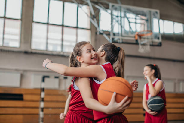 joueurs de basket-ball de filles étreignant sur la cour après le match - child basketball uniform sports uniform photos et images de collection