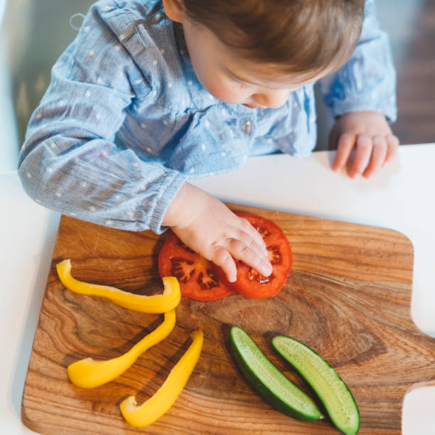 istock Baby's hand reaching for a tomato on a wooden plate 1143899934